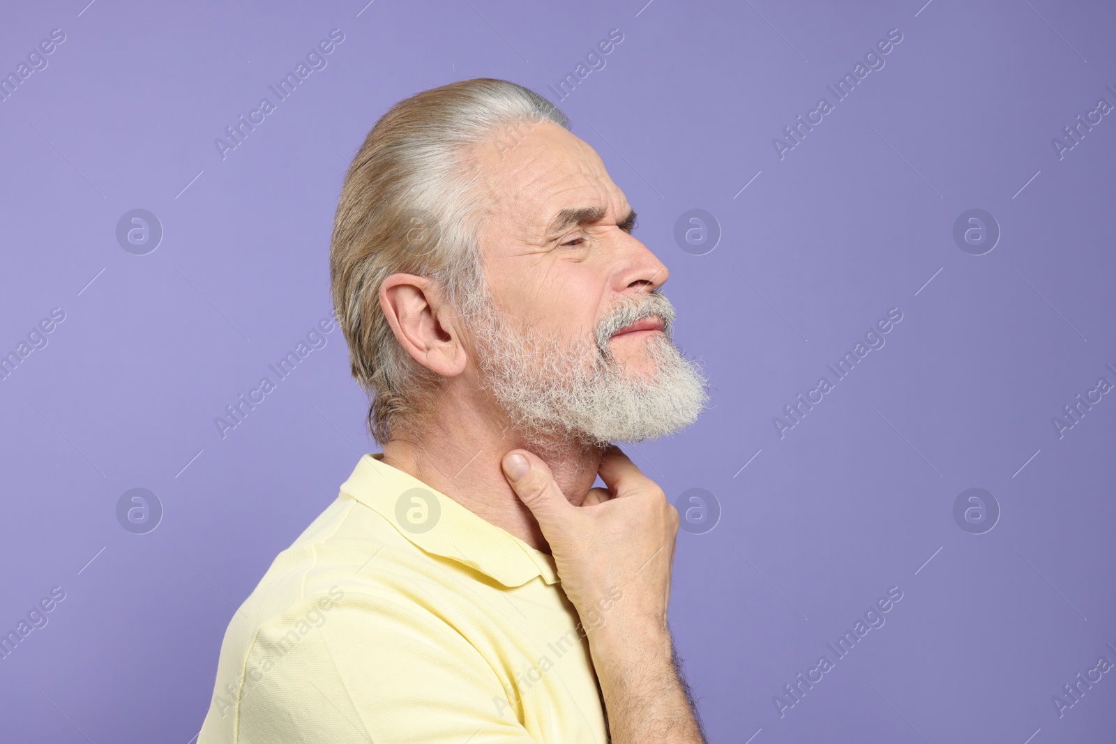 Photo of Senior man suffering from sore throat on light purple background. Cold symptoms