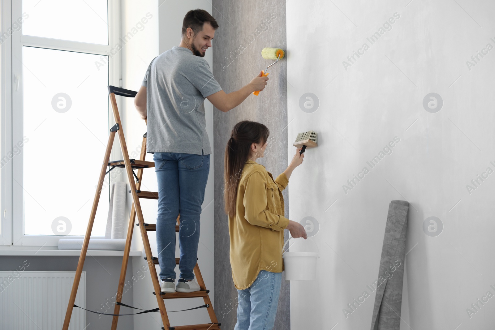 Photo of Woman and man hanging wallpaper in room