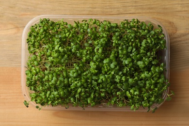 Photo of Sprouted arugula seeds in plastic container on wooden table, top view