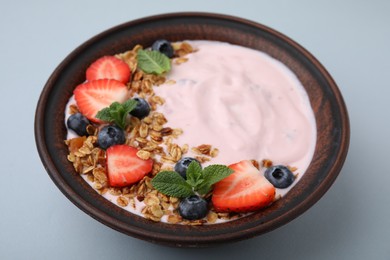 Photo of Bowl with yogurt, berries and granola on light grey background