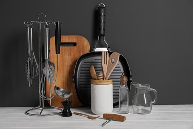 Photo of Set of different kitchen utensils on white wooden table against grey background