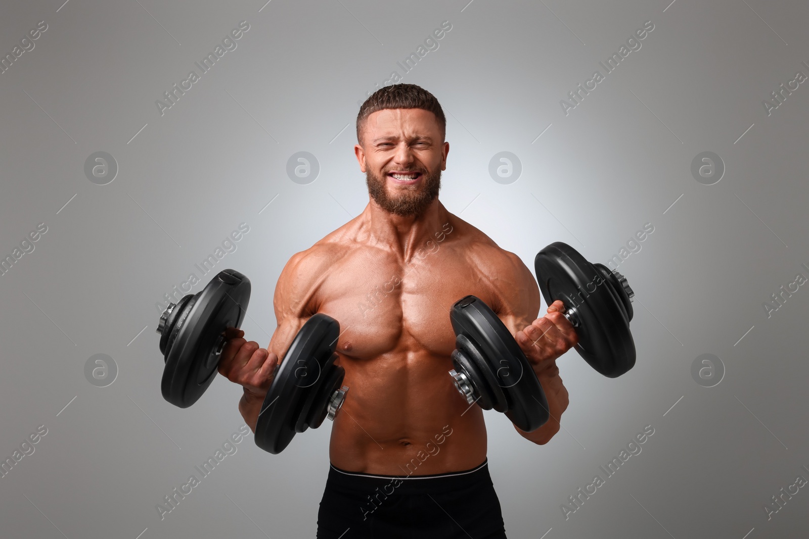 Photo of Emotional young bodybuilder exercising with dumbbells on light grey background