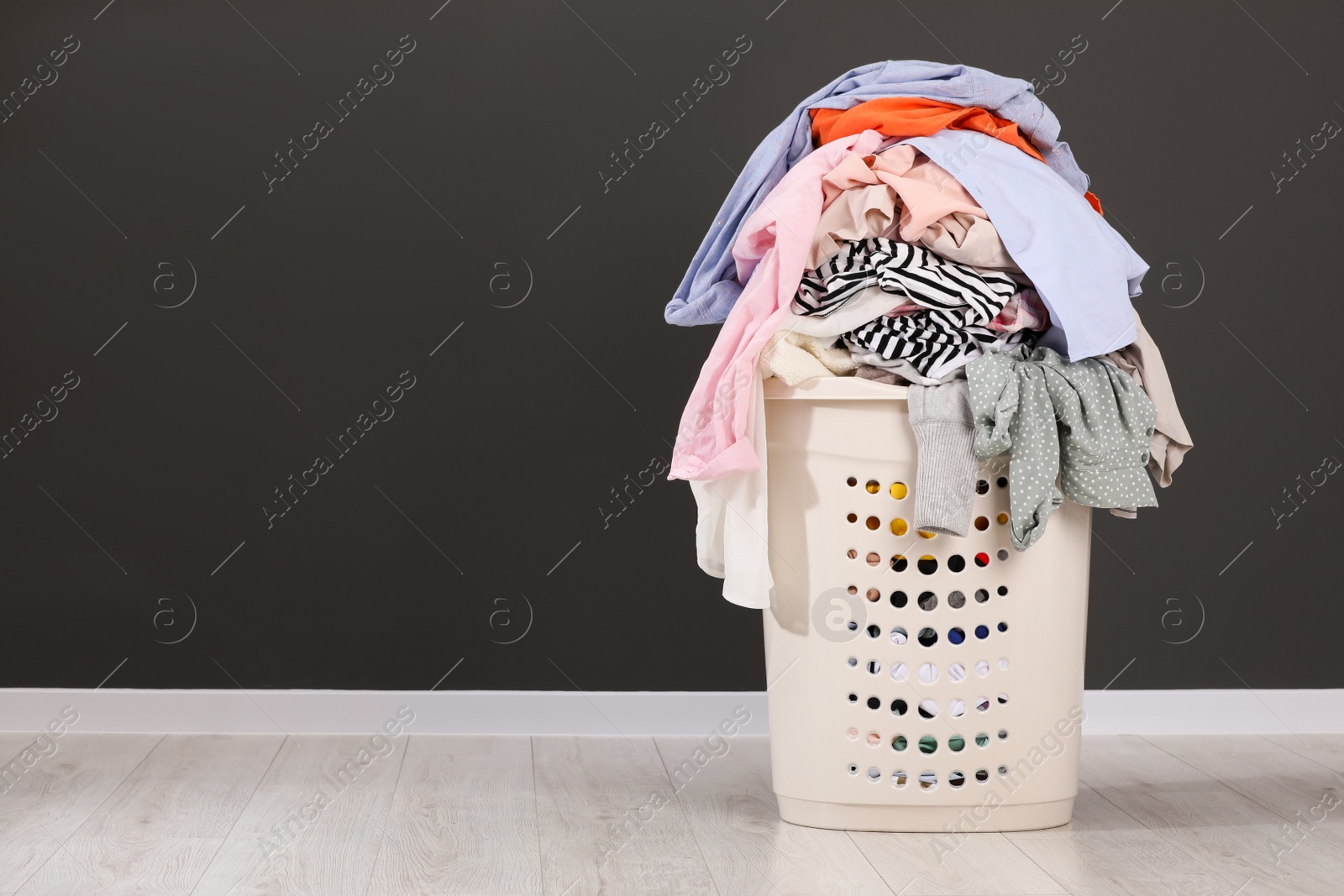 Photo of Laundry basket with clothes near dark grey wall. Space for text