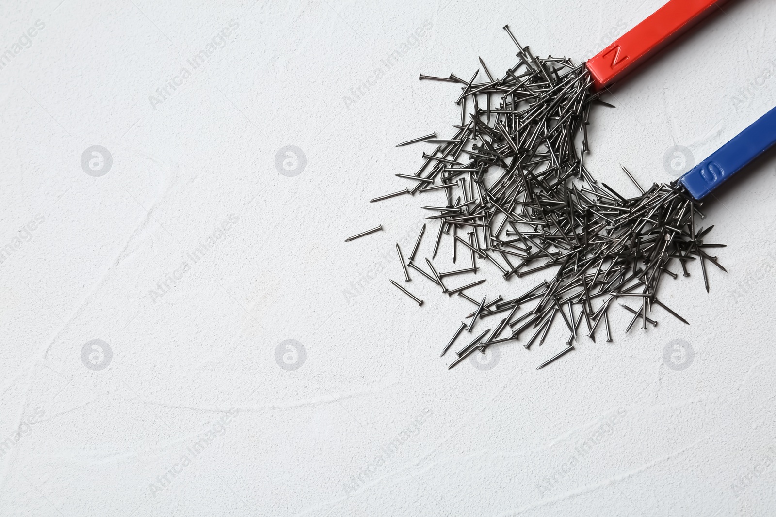 Photo of Magnet attracting nails on light background, top view with space for text