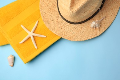 Photo of Straw hat, towel, starfish and shells on light blue background, flat lay with space for text. Beach accessories