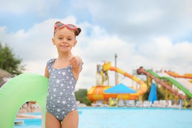 Cute little girl with inflatable ring near pool in water park, space for text