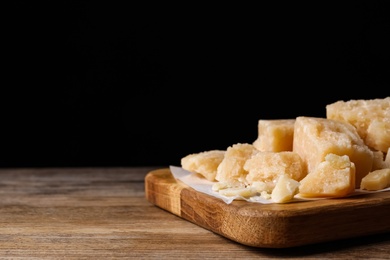 Photo of Pieces of delicious parmesan cheese on wooden table. Space for text