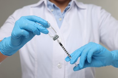 Doctor filling syringe with medication from glass vial on grey background, closeup