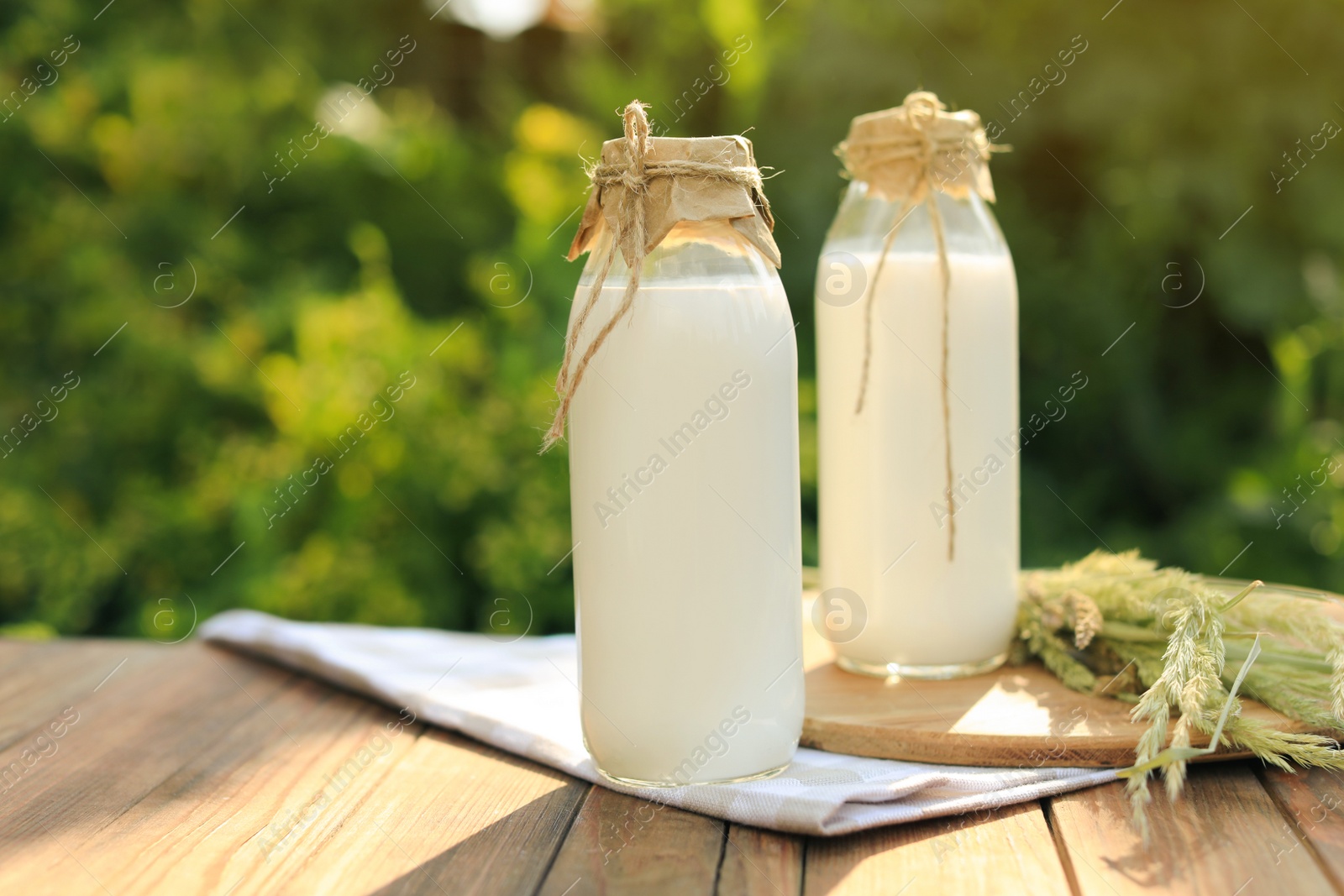 Photo of Bottles of tasty fresh milk on wooden table outdoors, space for text