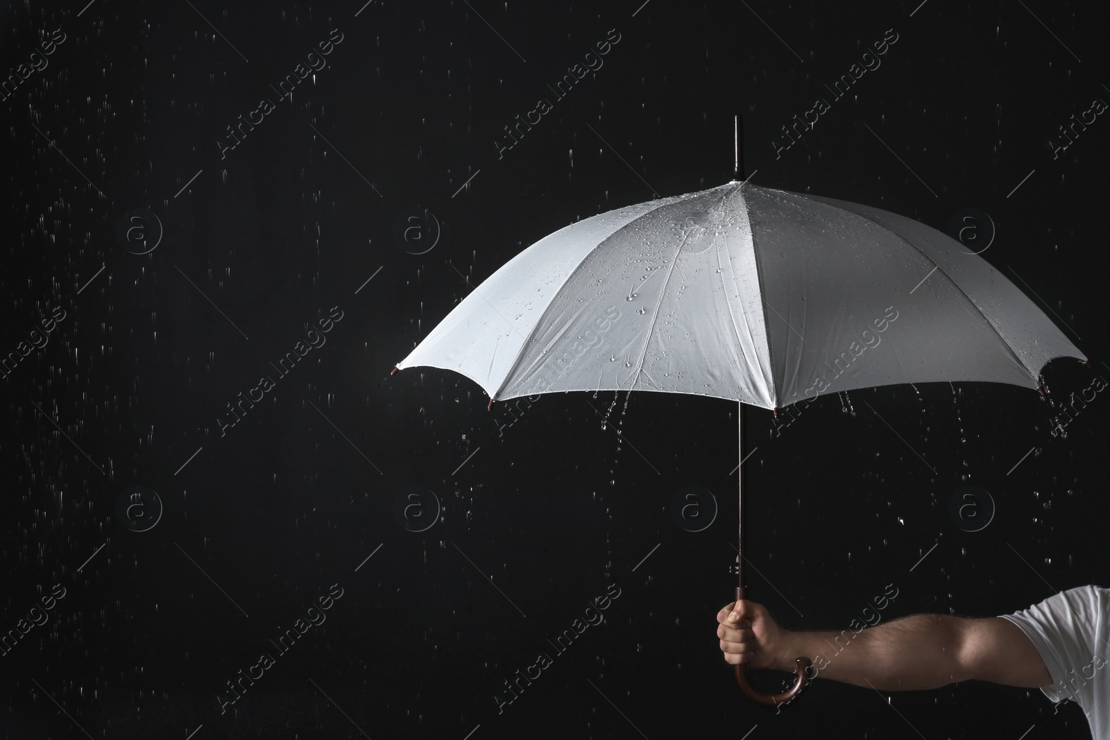 Photo of Man holding opened white umbrella under rain against black background, closeup