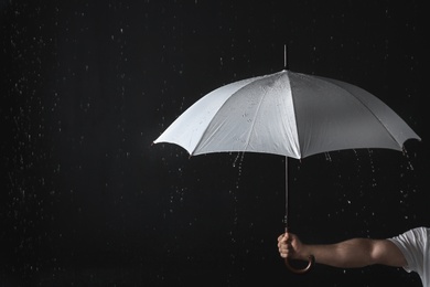 Photo of Man holding opened white umbrella under rain against black background, closeup