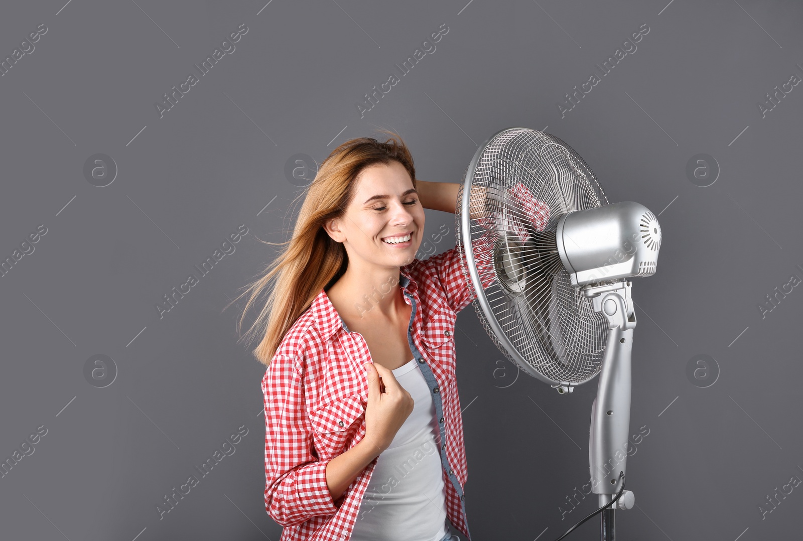 Photo of Woman refreshing from heat in front of fan on grey background