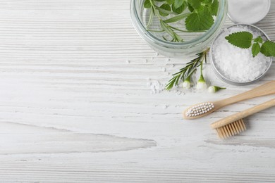 Flat lay composition with toothbrushes and herbs on white wooden table. Space for text