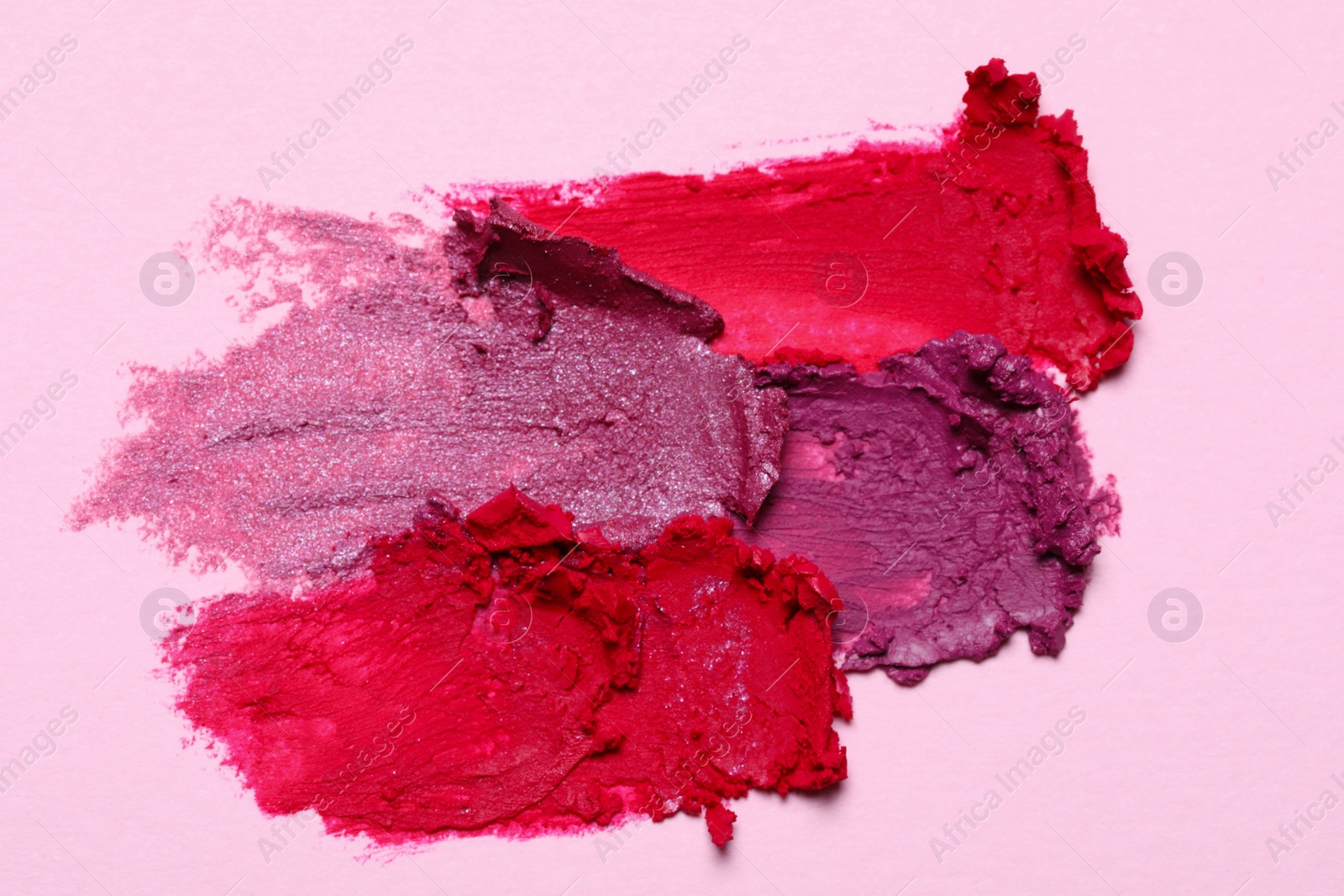 Photo of Smears of bright lipsticks on pink background, top view