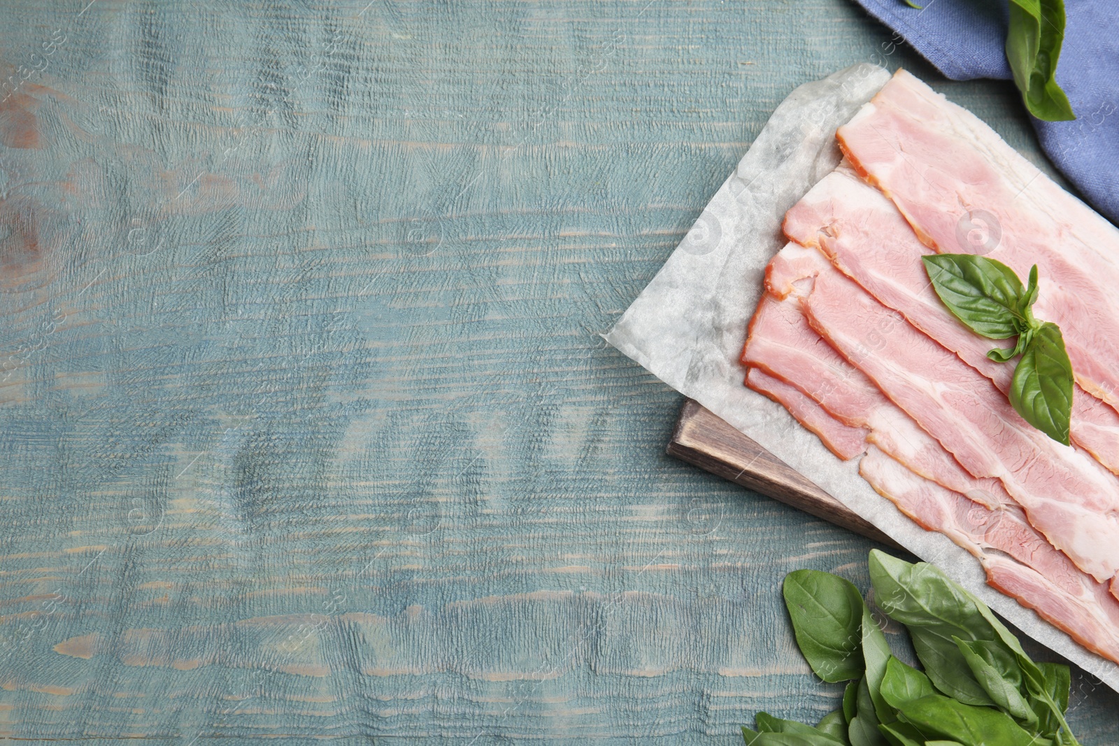 Photo of Flat lay composition with sliced raw bacon on light blue wooden table. Space for text