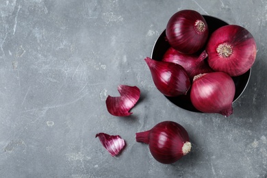 Photo of Metal bowl with ripe red onions on grey table, top view. Space for text