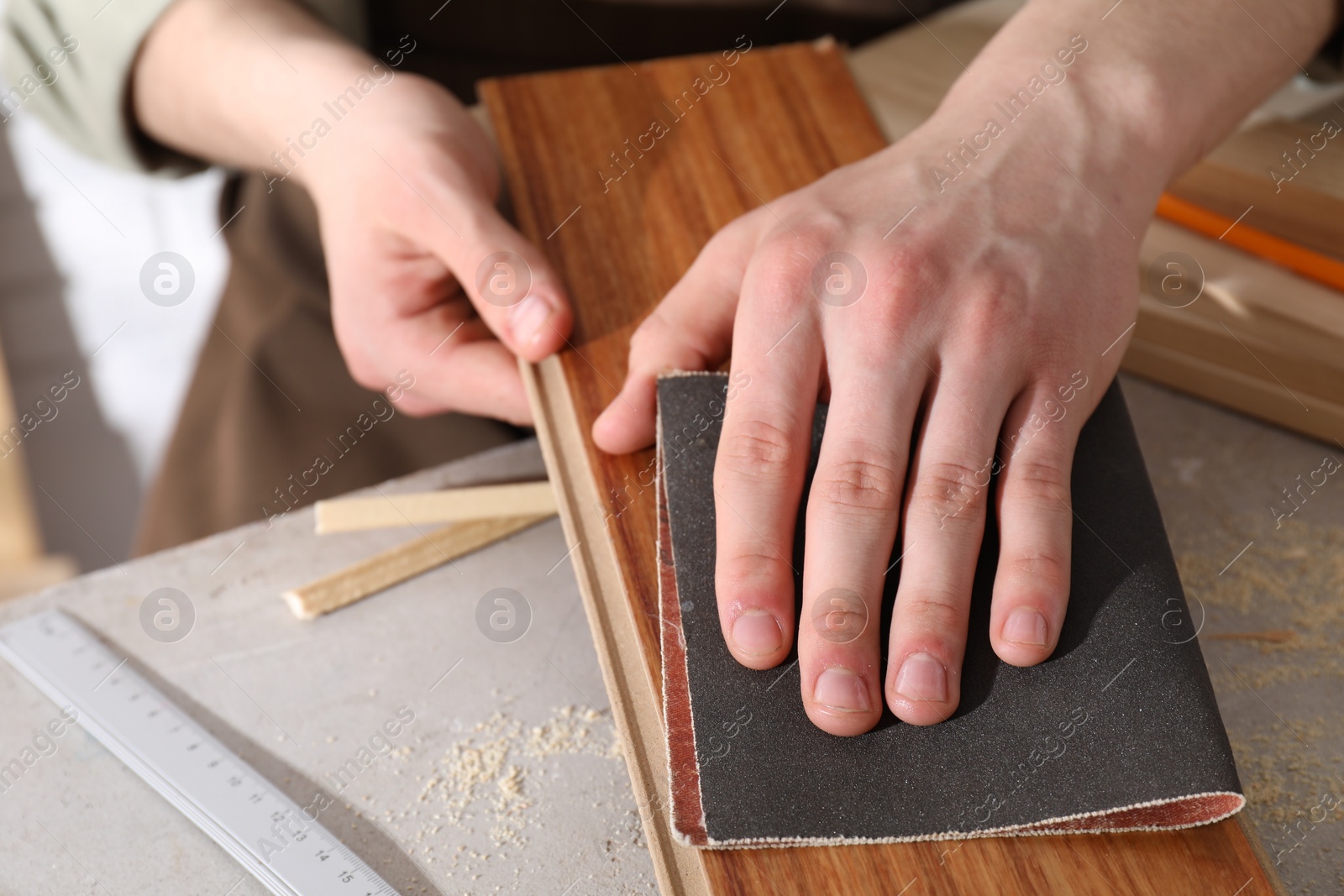 Photo of Man polishing wooden plank with sandpaper at grey table indoors, closeup