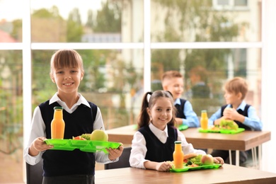 Photo of Happy girl holding tray with healthy food in school canteen