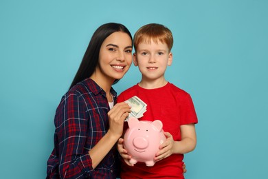 Photo of Mother and her son putting money into piggy bank on light blue background