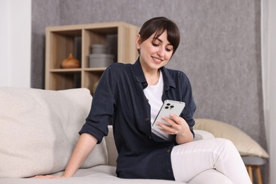 Photo of Beautiful young housewife using smartphone on sofa at home