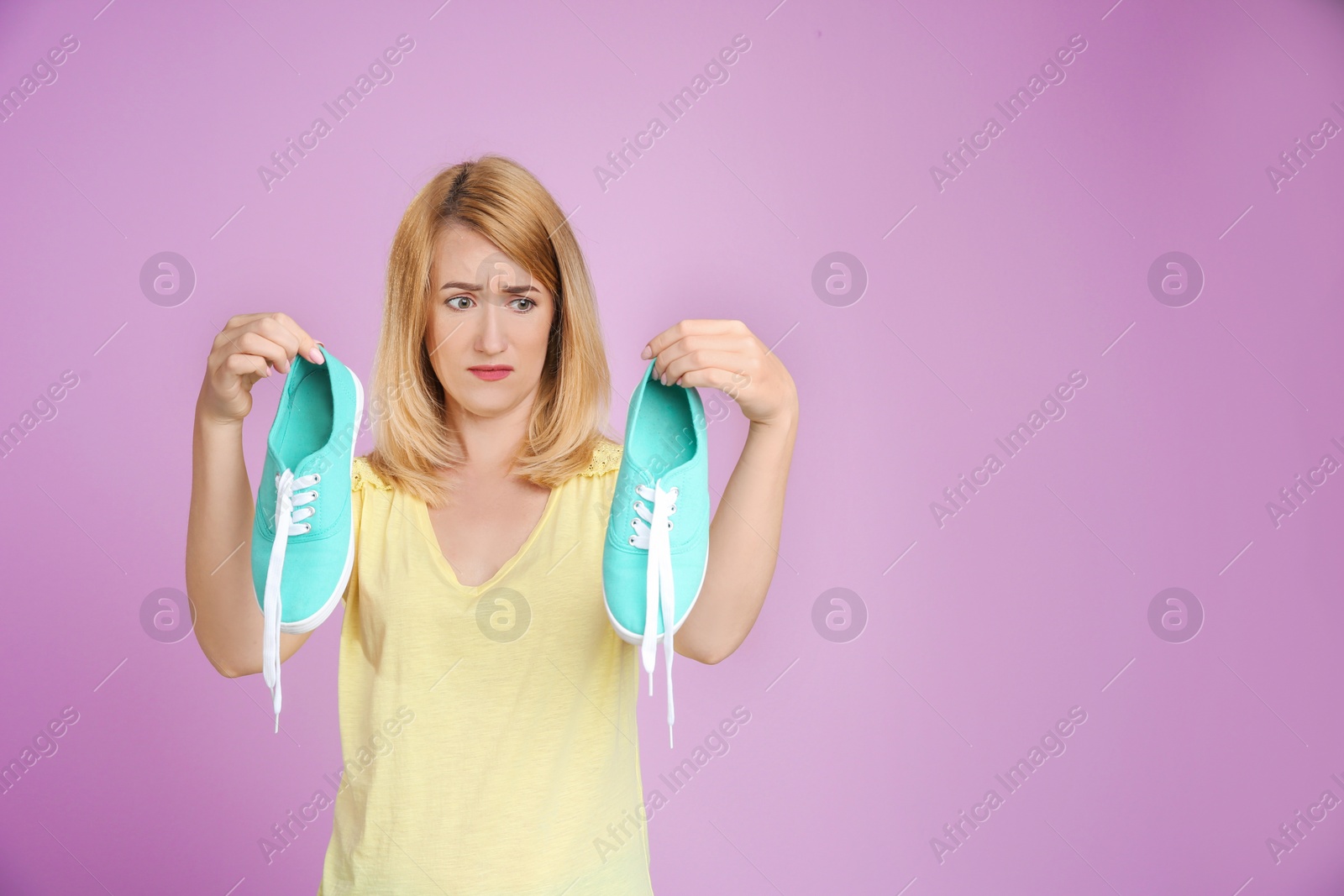 Photo of Young woman with stinky shoes on color background. Air freshener