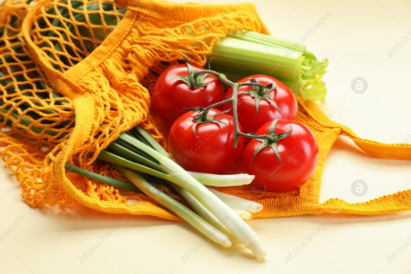 Photo of String bag with different vegetables on beige background, closeup