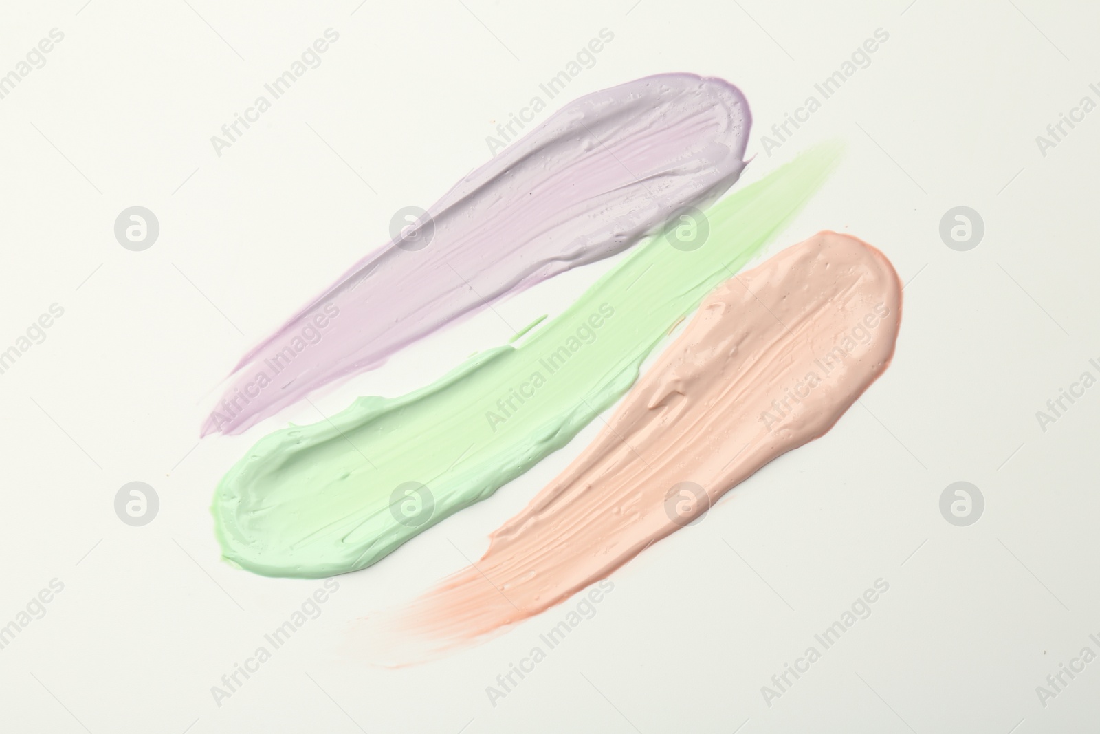 Photo of Strokes of pink, green and purple color correcting concealers on white background, top view