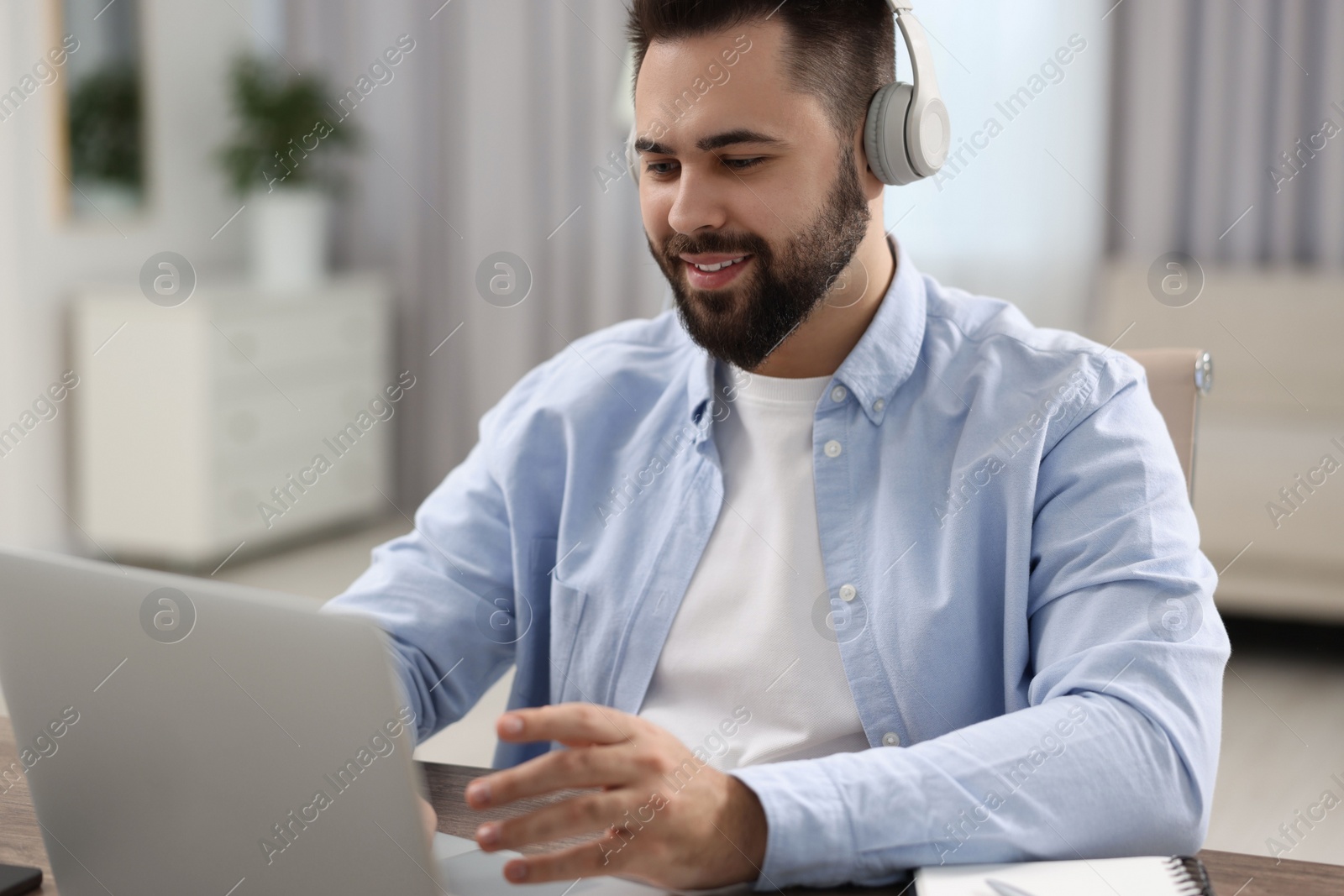 Photo of Young man in headphones watching webinar at table in room