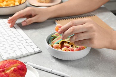 Photo of Bad habits. Woman eating jelly candies while working on computer at grey marble table, closeup