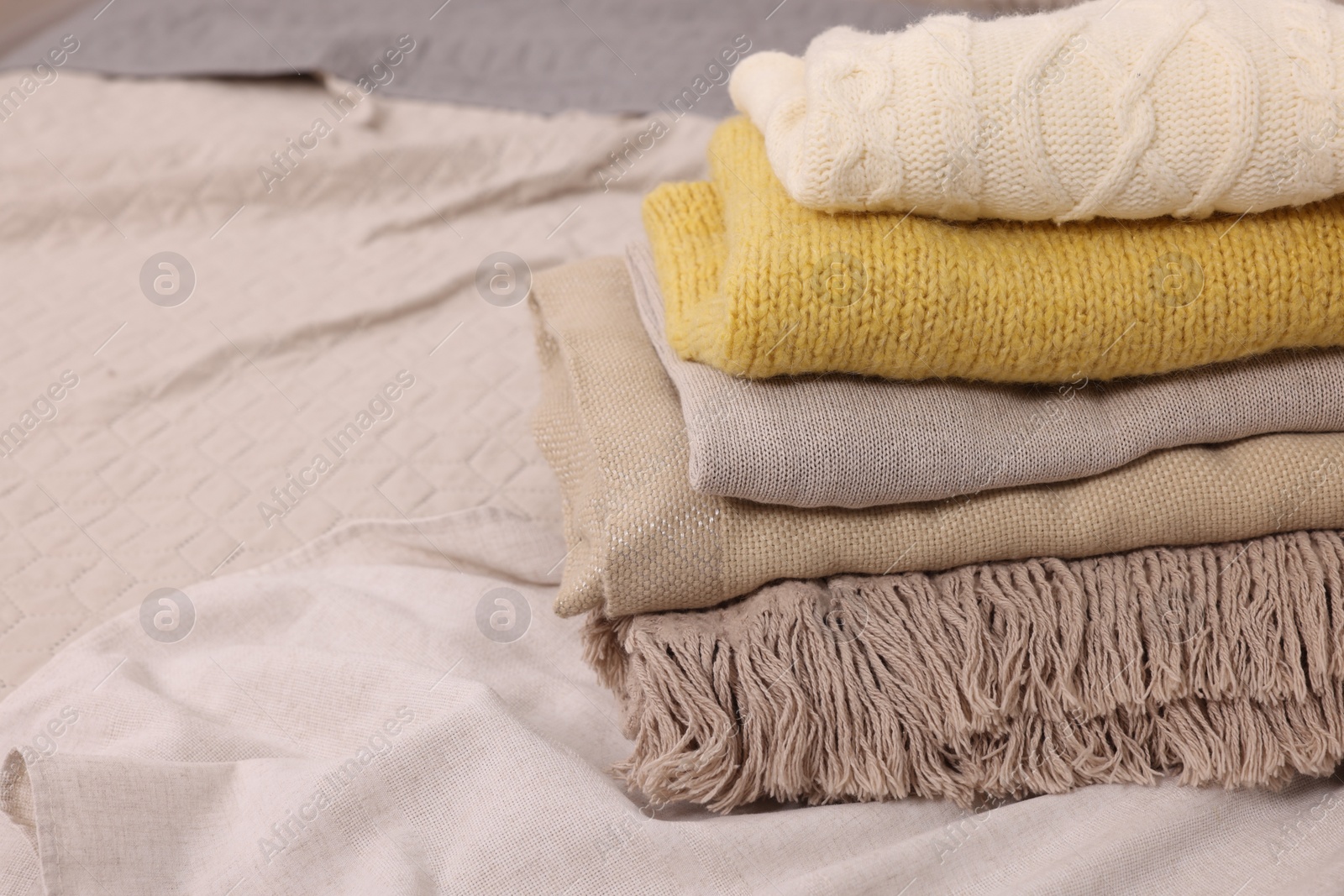 Photo of Stack of different folded blankets and clothes on bed, closeup with space for text. Home textile