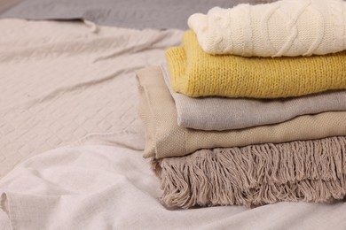 Stack of different folded blankets and clothes on bed, closeup with space for text. Home textile