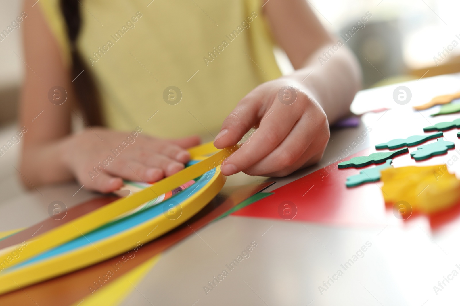 Photo of Little girl quilling at table indoors, closeup. Creative hobby