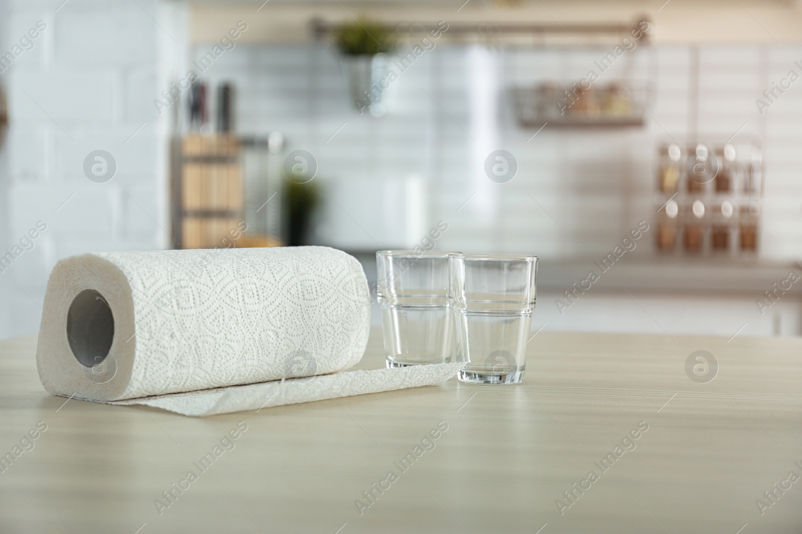 Photo of Roll of paper towels and glasses on table in kitchen. Space for text