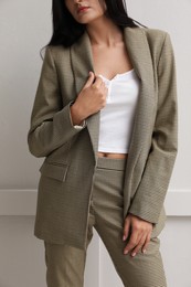 Woman in formal suit near light grey wall, closeup. Business attire