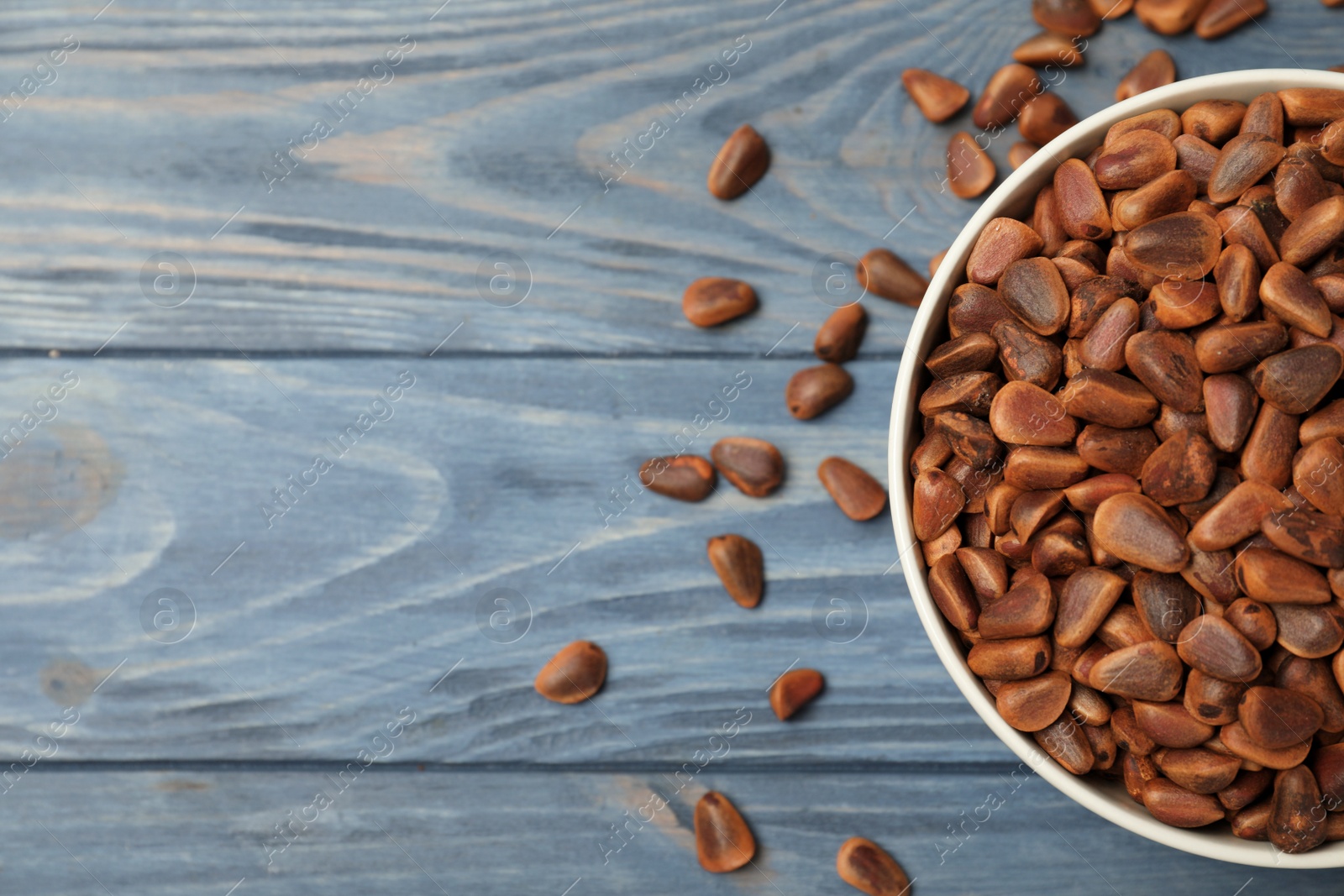 Photo of Bowl with pine nuts and space for text on wooden background, top view