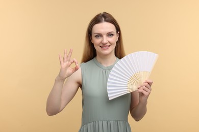 Photo of Happy woman with hand fan showing OK gesture on beige background