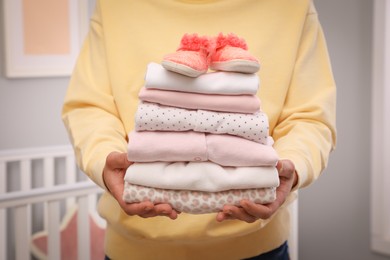 Photo of Woman holding stack of girl's clothes and booties indoors, closeup