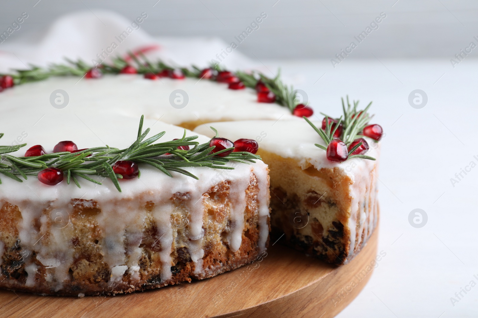 Photo of Traditional Christmas cake decorated with rosemary and pomegranate seeds on white table, closeup