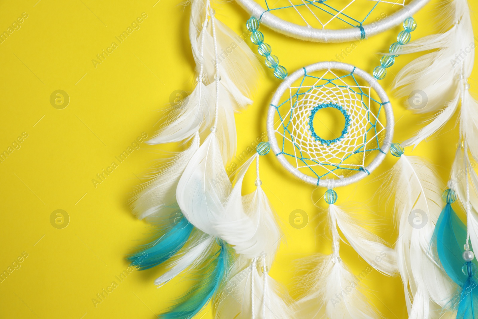 Photo of Beautiful dream catcher hanging on yellow background, closeup