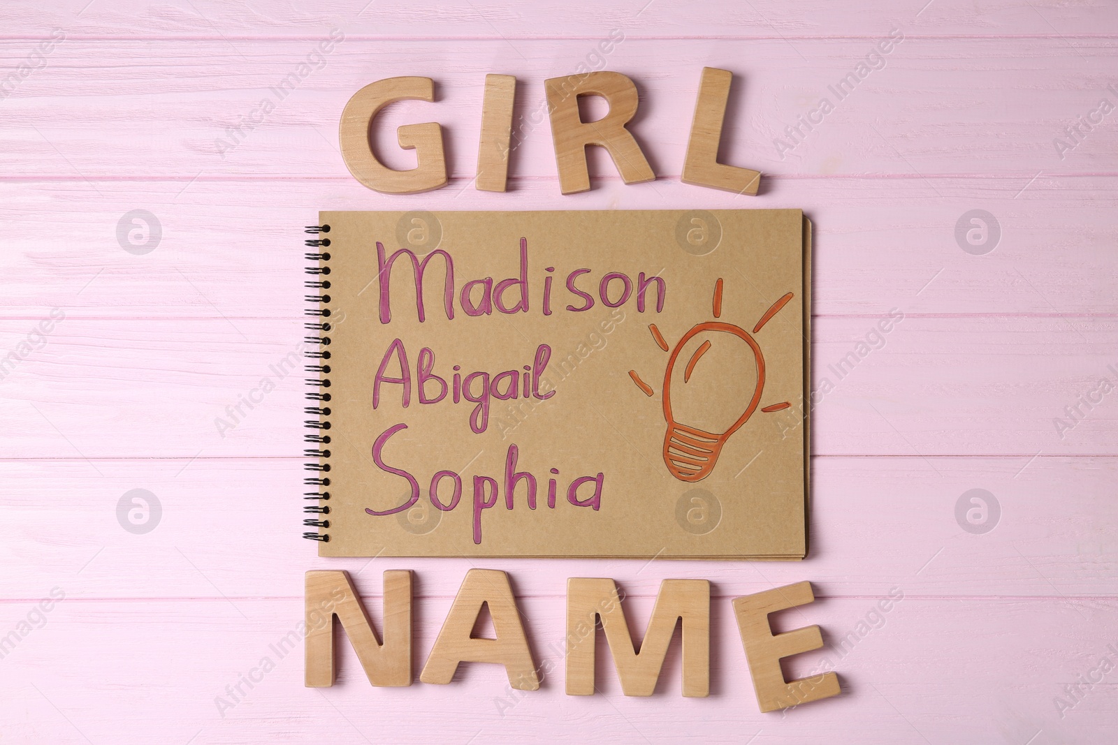 Photo of Notebook with written different baby names and wooden letters on pink wooden background, flat lay