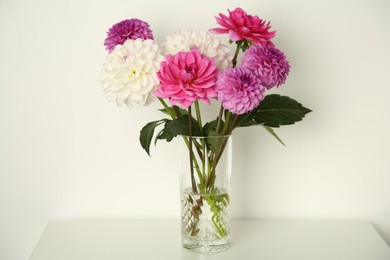 Photo of Bouquet of beautiful Dahlia flowers in vase on table near white wall