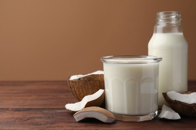 Bottle and glass of delicious vegan milk near coconut pieces on wooden table, space for text