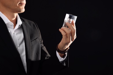 Young man with perfume bottle on black background, closeup