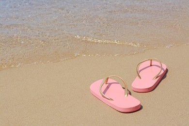 Photo of Stylish pink flip flops on wet sand near sea, space for text