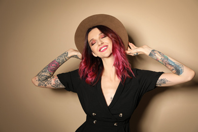 Photo of Beautiful woman with tattoos on arms against beige background