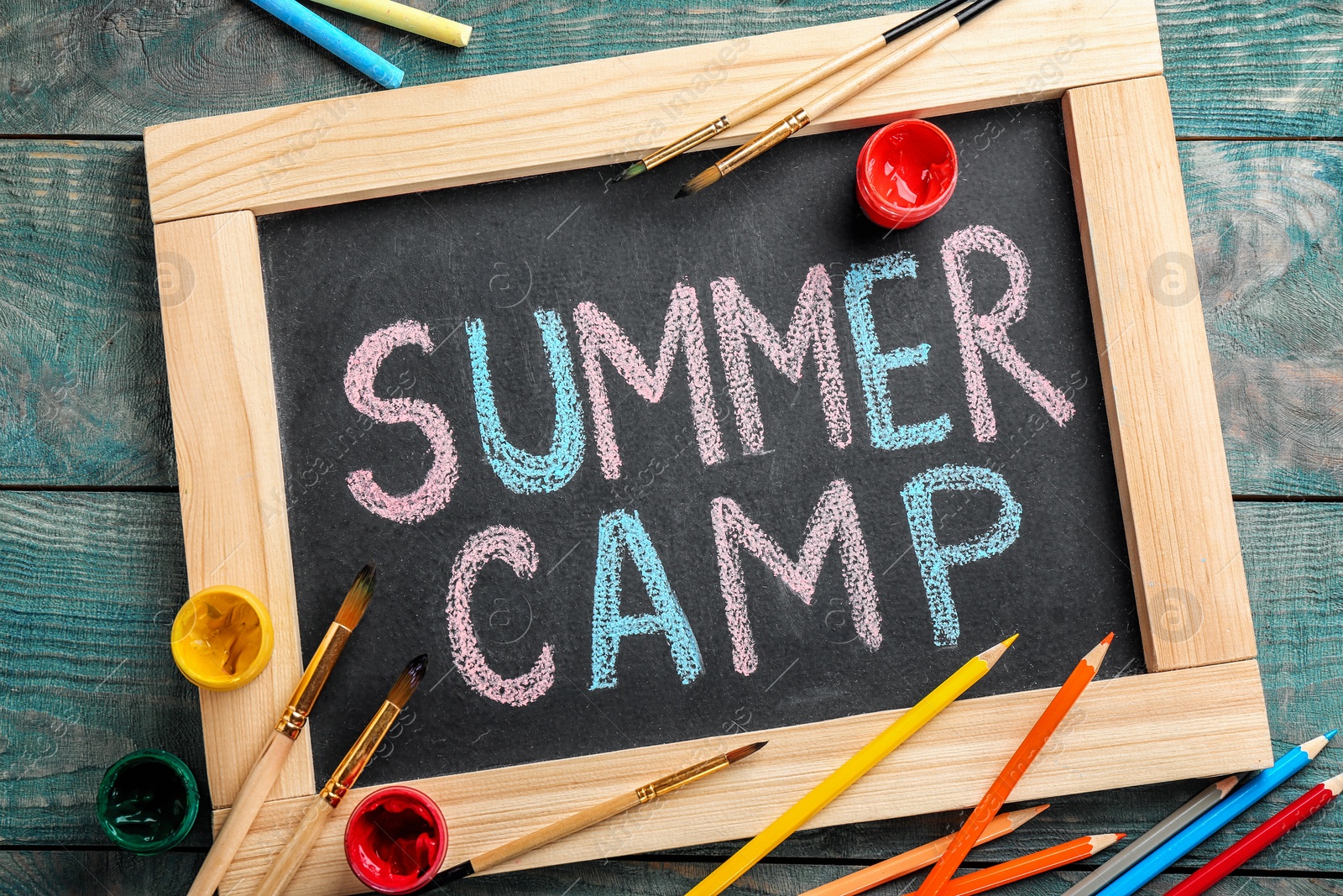 Photo of Text "SUMMER CAMP" on chalkboard, brushes and paints, top view