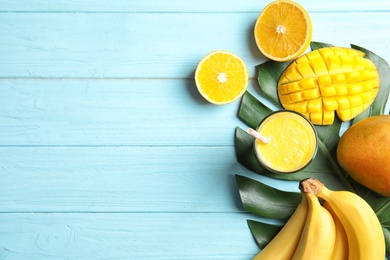 Glass of fresh mango drink and tropical fruits on color wooden background, top view. Space for text