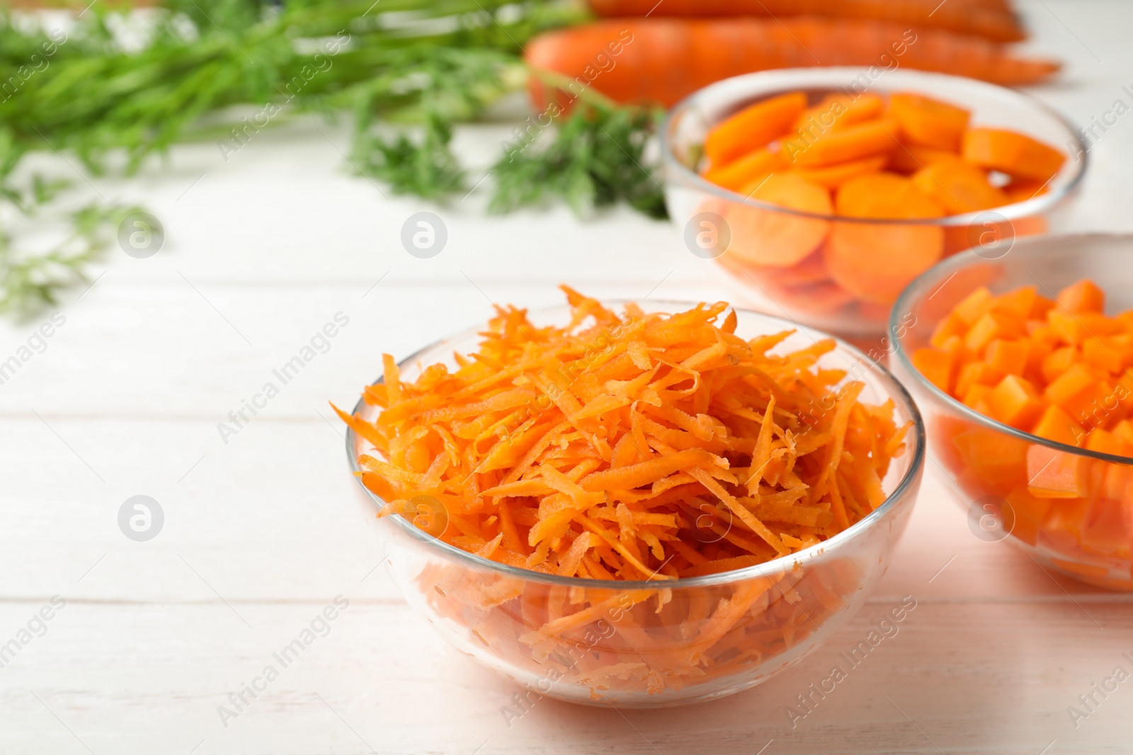 Photo of Bowls of differently cut carrots on white background