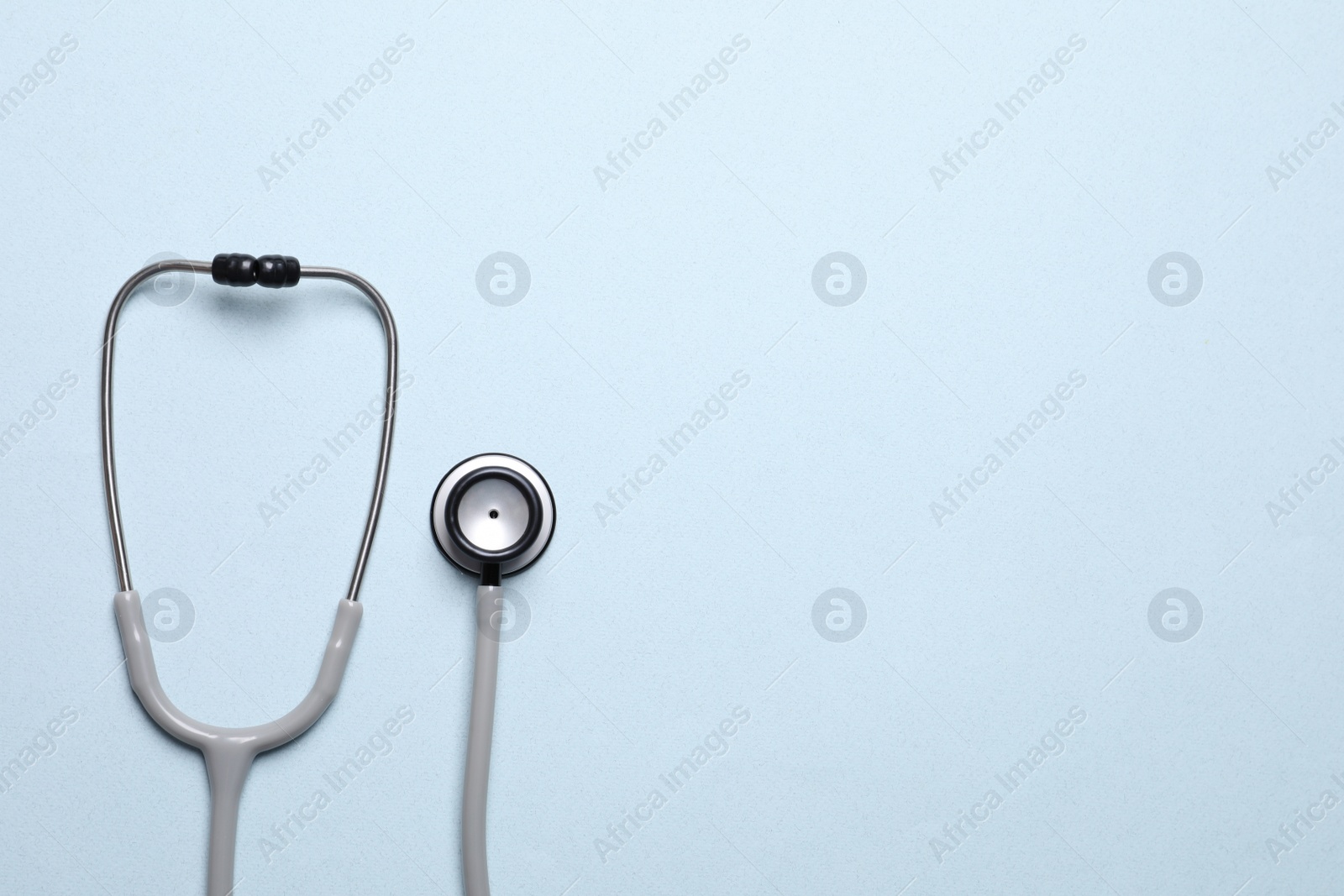 Photo of Stethoscope on light blue background, top view. Space for text