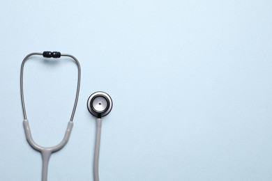 Stethoscope on light blue background, top view. Space for text